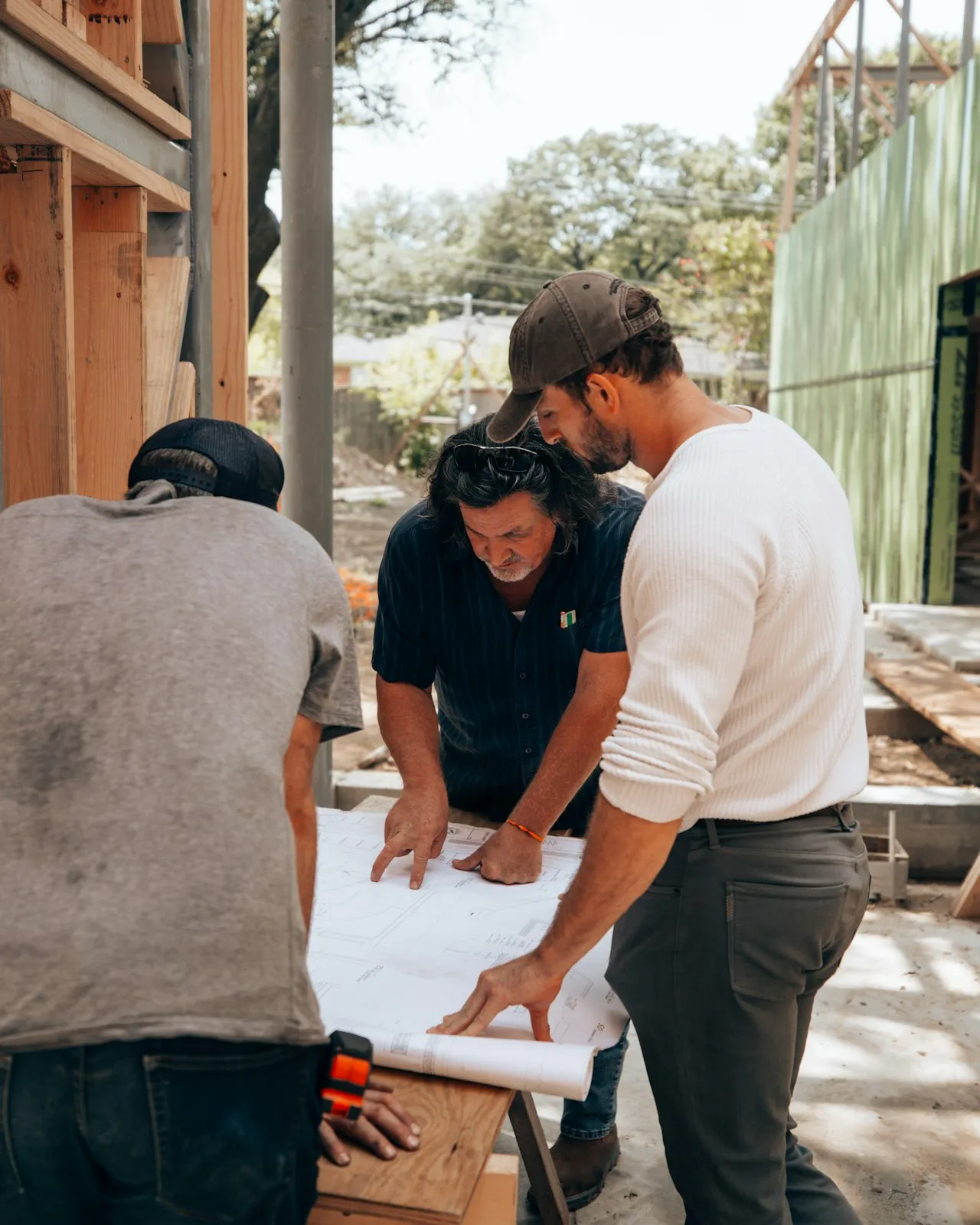 Three builders looking over plans on a timber frame site.