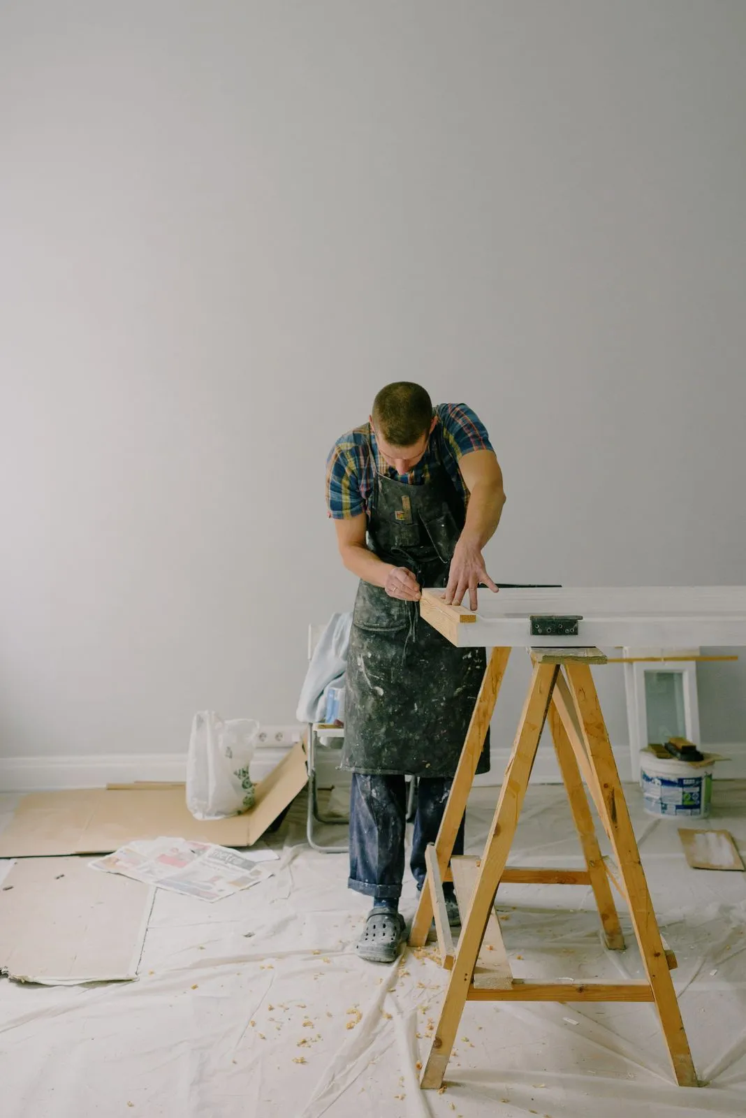 A carpenter working at a sawhorse in a room being renovated.