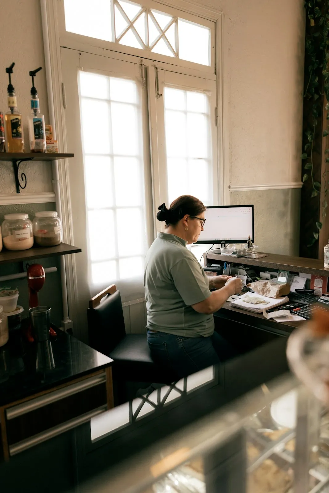 A shop owner working through paperwork at her counter computer.